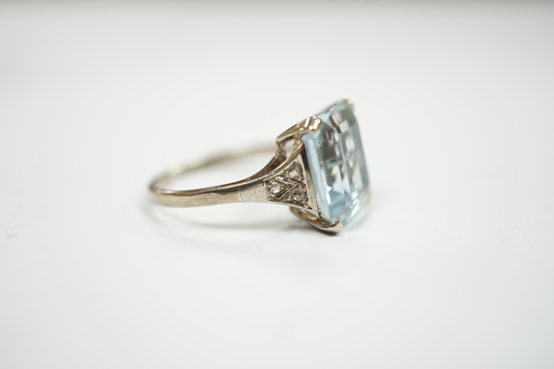 A white metal and single stone emerald cut aquamarine set ring, with rose cut diamond chip set shoulders (one stone missing), size M, gross weight 3.2 grams.